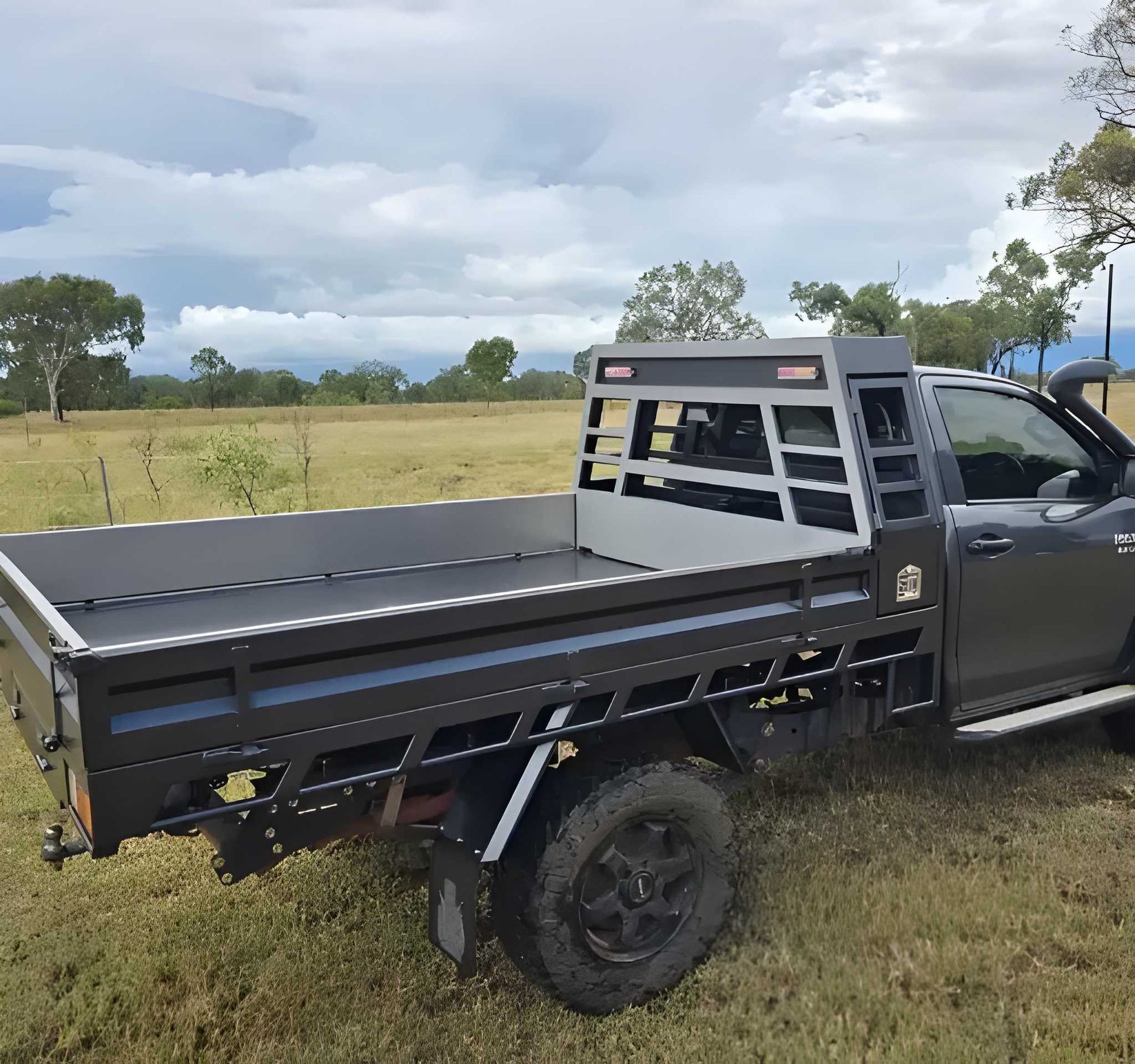 Dark Grey Flatbed Truck With Black Tires and Metal Tray in a Field — GC Custom Fabrication in Molendinar, QLD