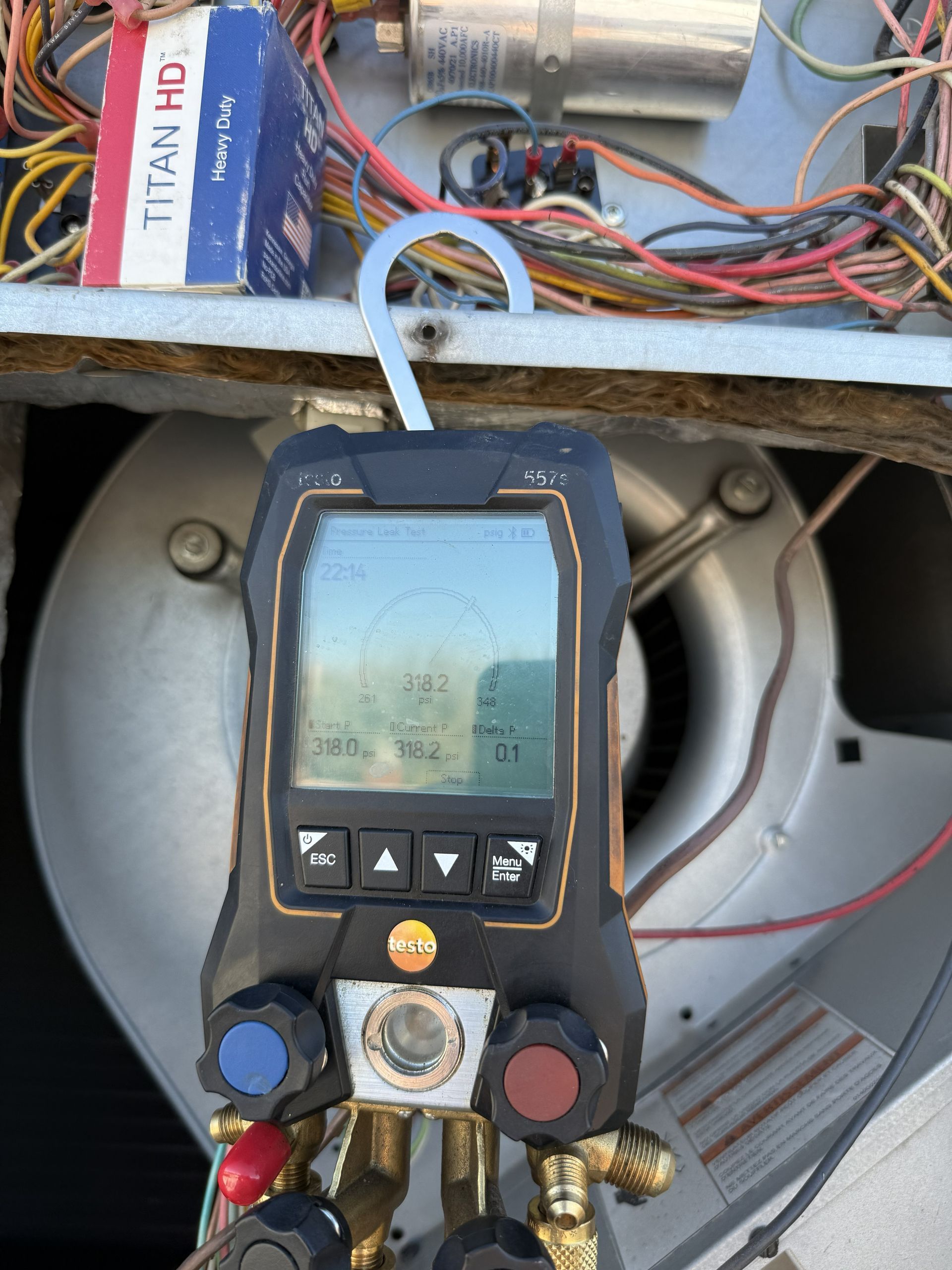 HVAC gauge displaying readings, held near a blower fan inside an air conditioning unit.