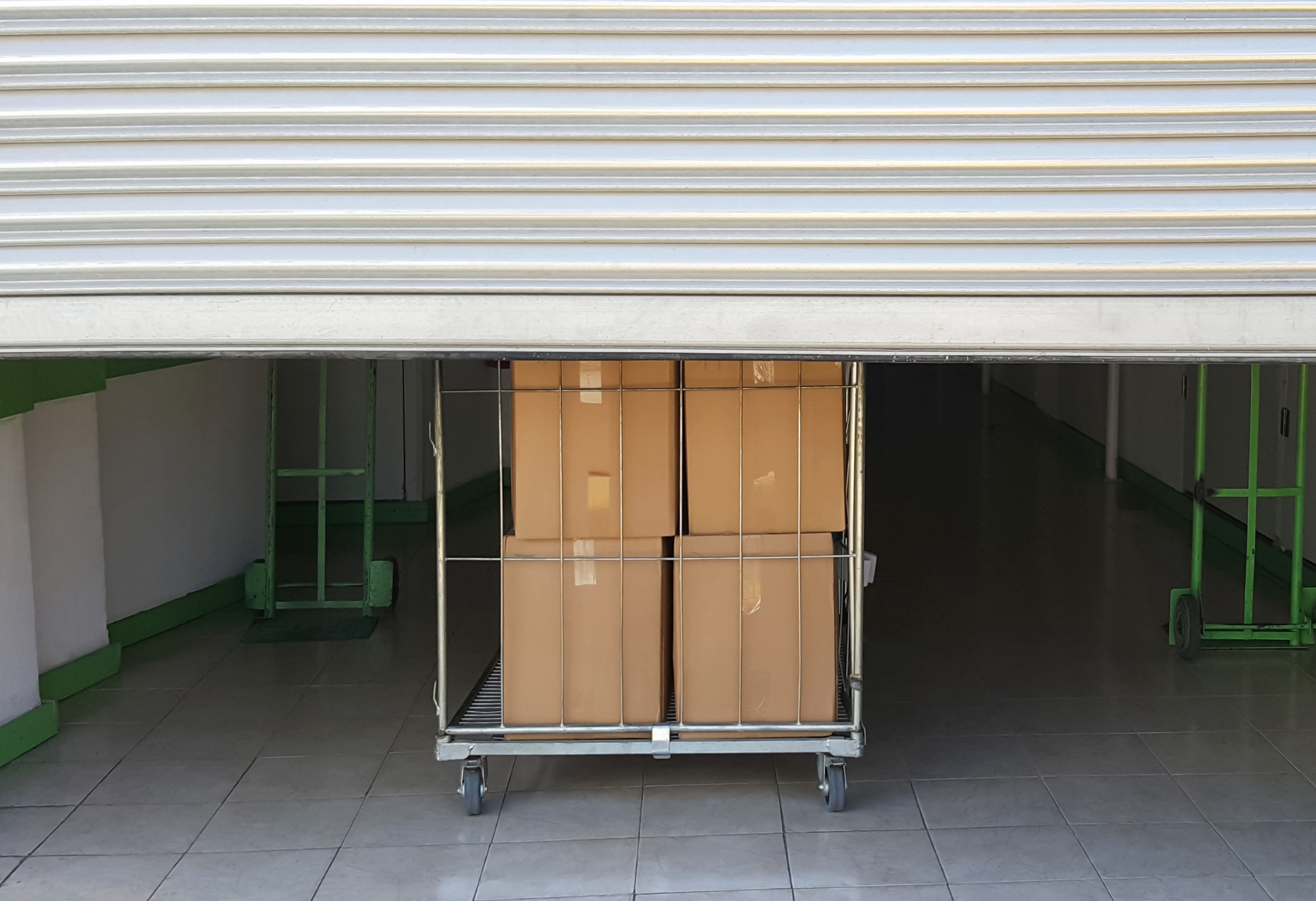 Boxes on a cart inside a warehouse being loaded or unloaded under a partially open metal shutter door.