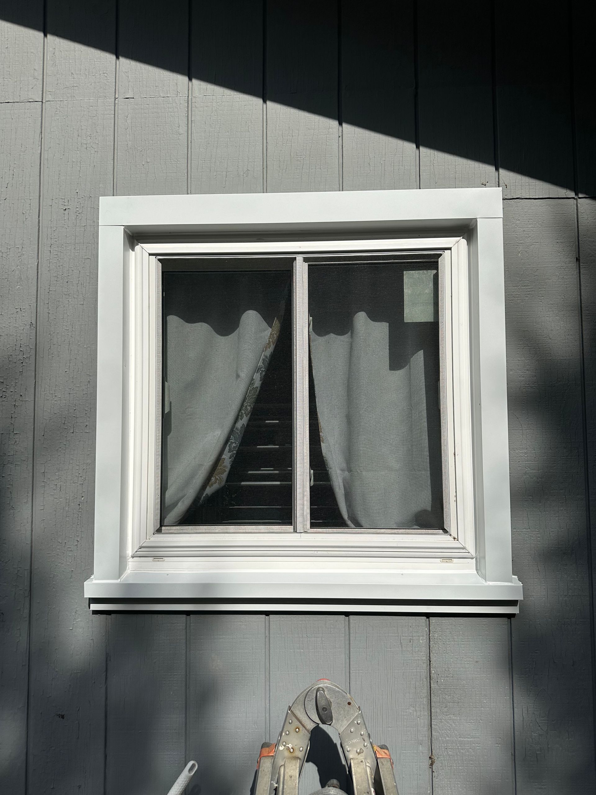 A white window on a gray wall with a ladder in front of it
