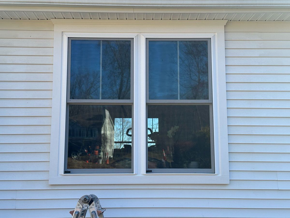 A white house with two windows and a ladder in front of it.