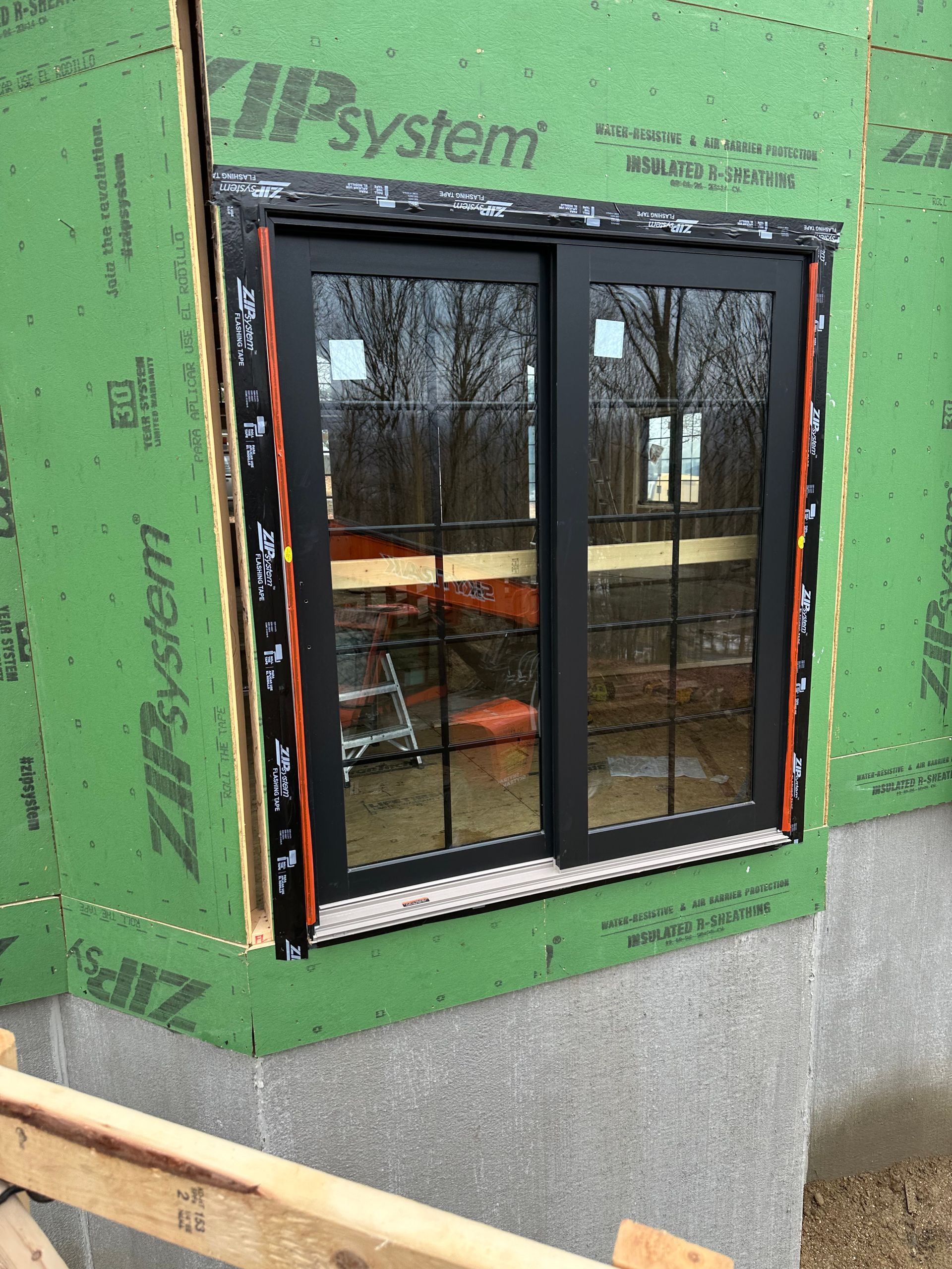 A window with a black frame is surrounded by green zipsystem insulation