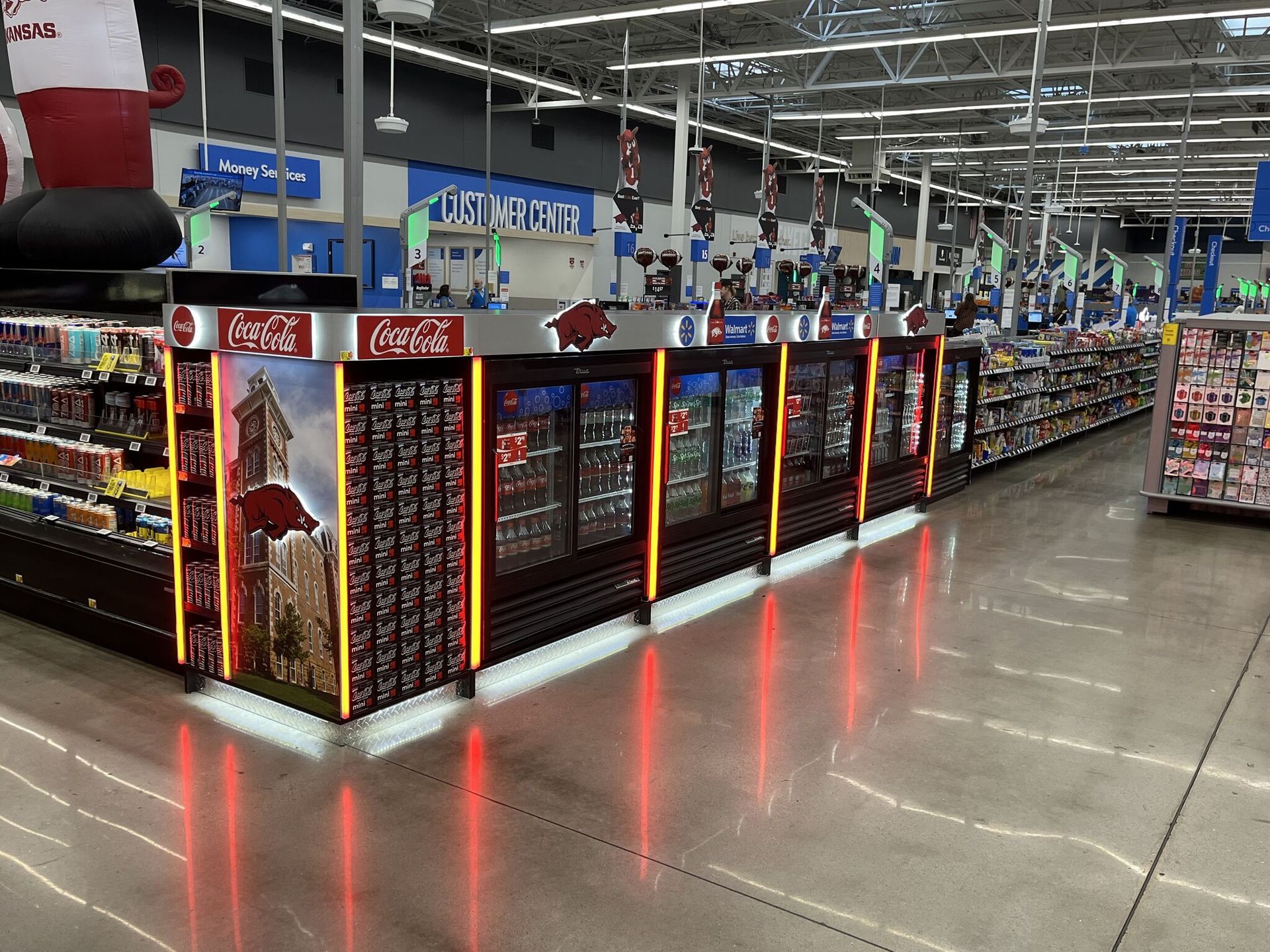 Inside a store, a long Coca-Cola display with coolers and illuminated edges.