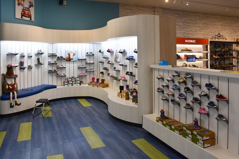 Shoe store interior with curved display shelves, shoes, blue flooring, and a child's toy.