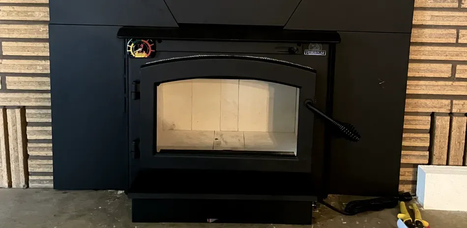 A wood stove is sitting in front of a brick fireplace.