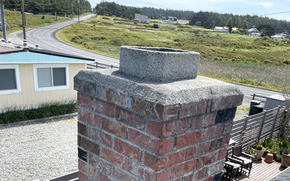 A brick chimney with a view of a road and a house in the background.