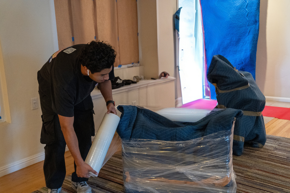 A man is wrapping a box with plastic wrap in a kitchen.