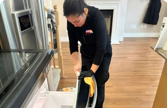 A woman is cleaning a refrigerator in a kitchen.