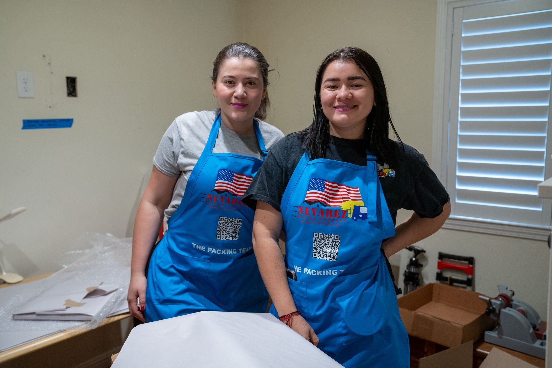 Two women wearing blue aprons are standing next to each other in a room.