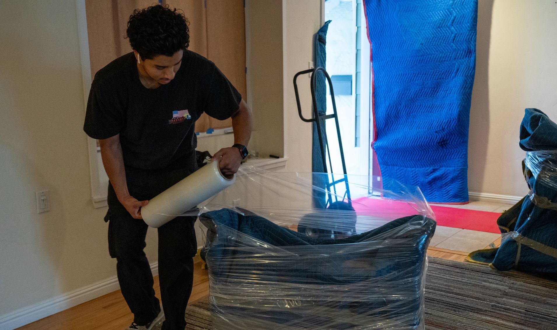 A man is wrapping a chair in plastic wrap in a living room.