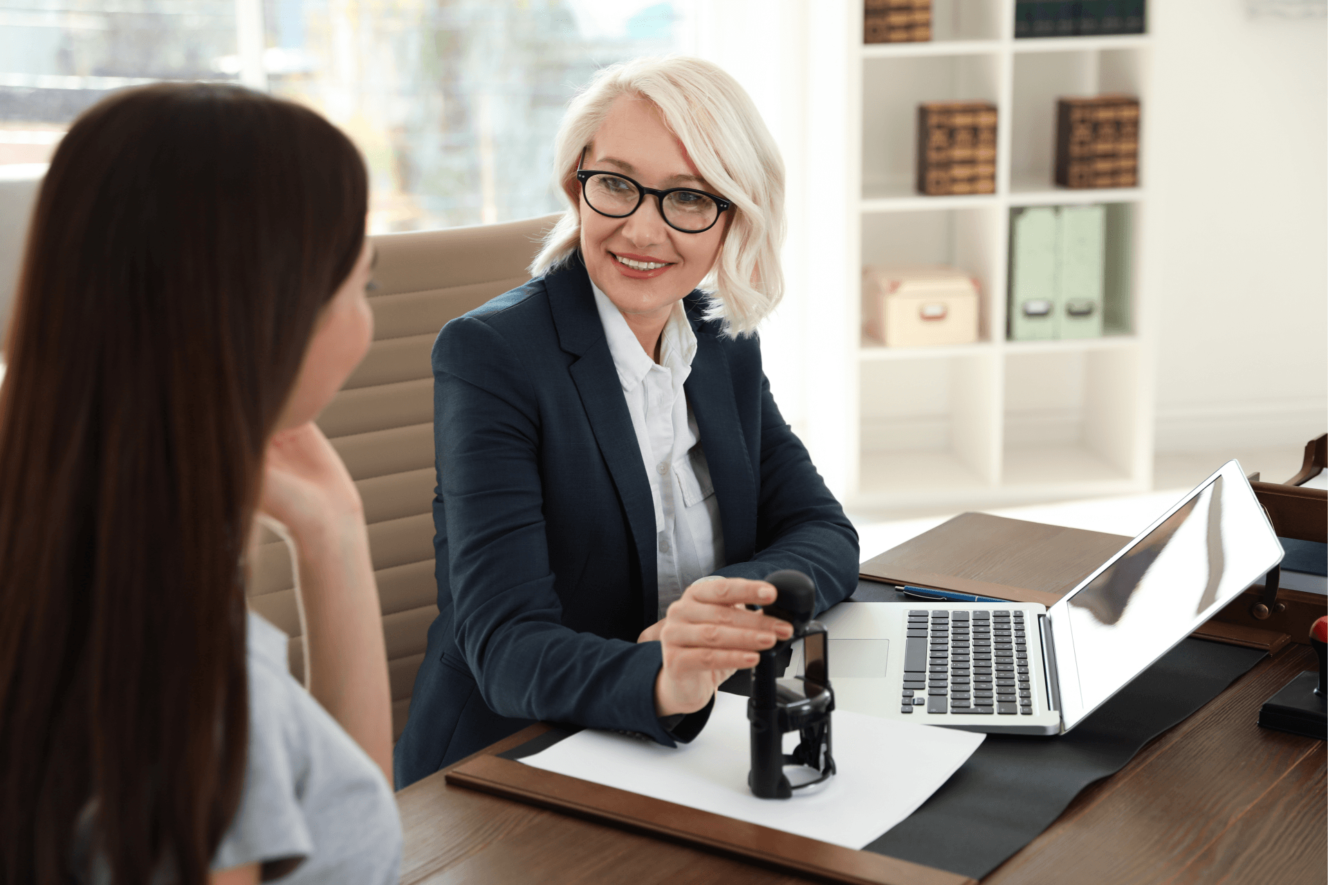 A woman is sitting at a desk talking to another woman.