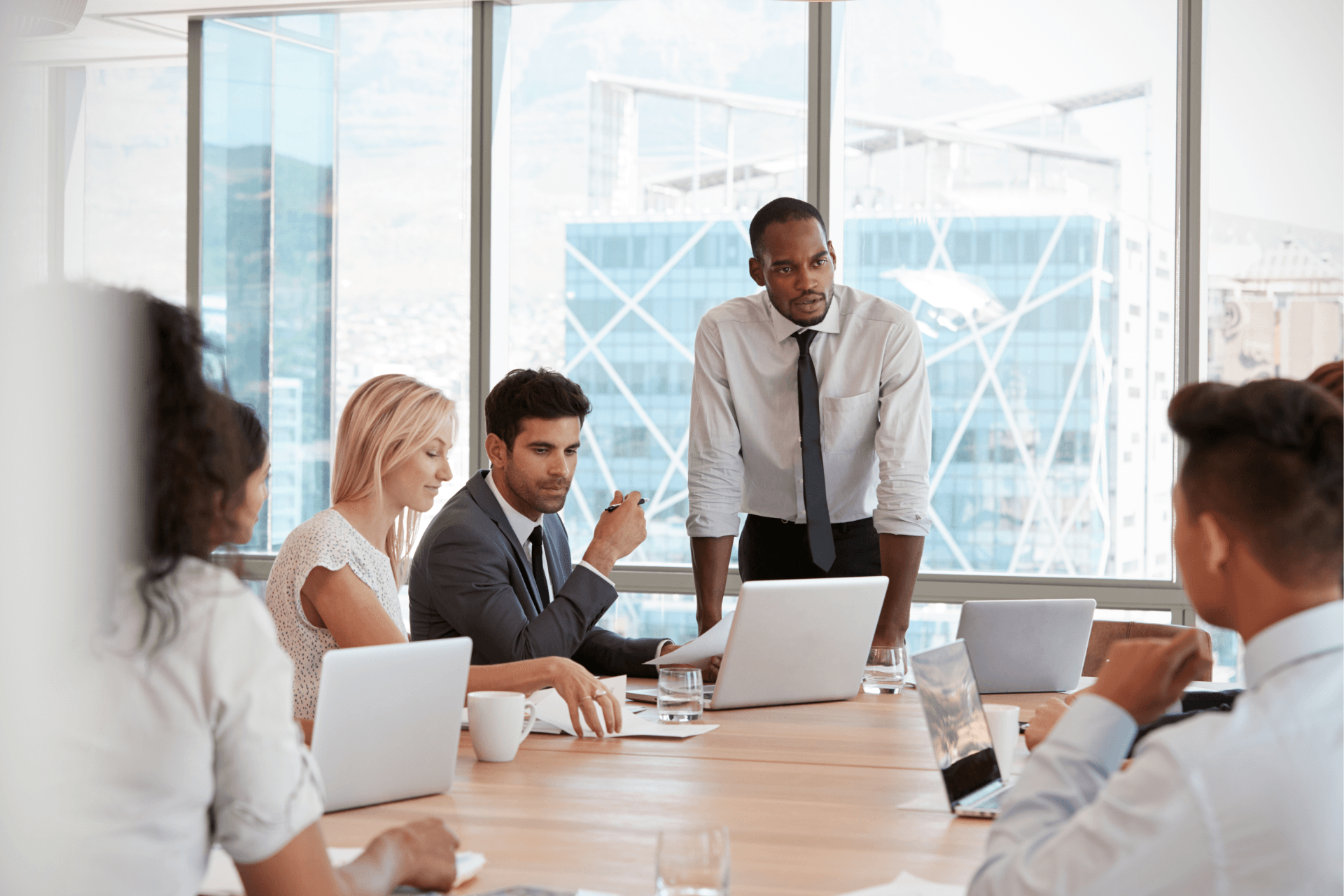 A group of business people are sitting around a conference table with laptops.