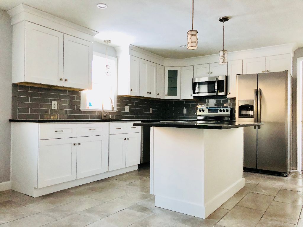 A kitchen with white cabinets , stainless steel appliances , and a large island.