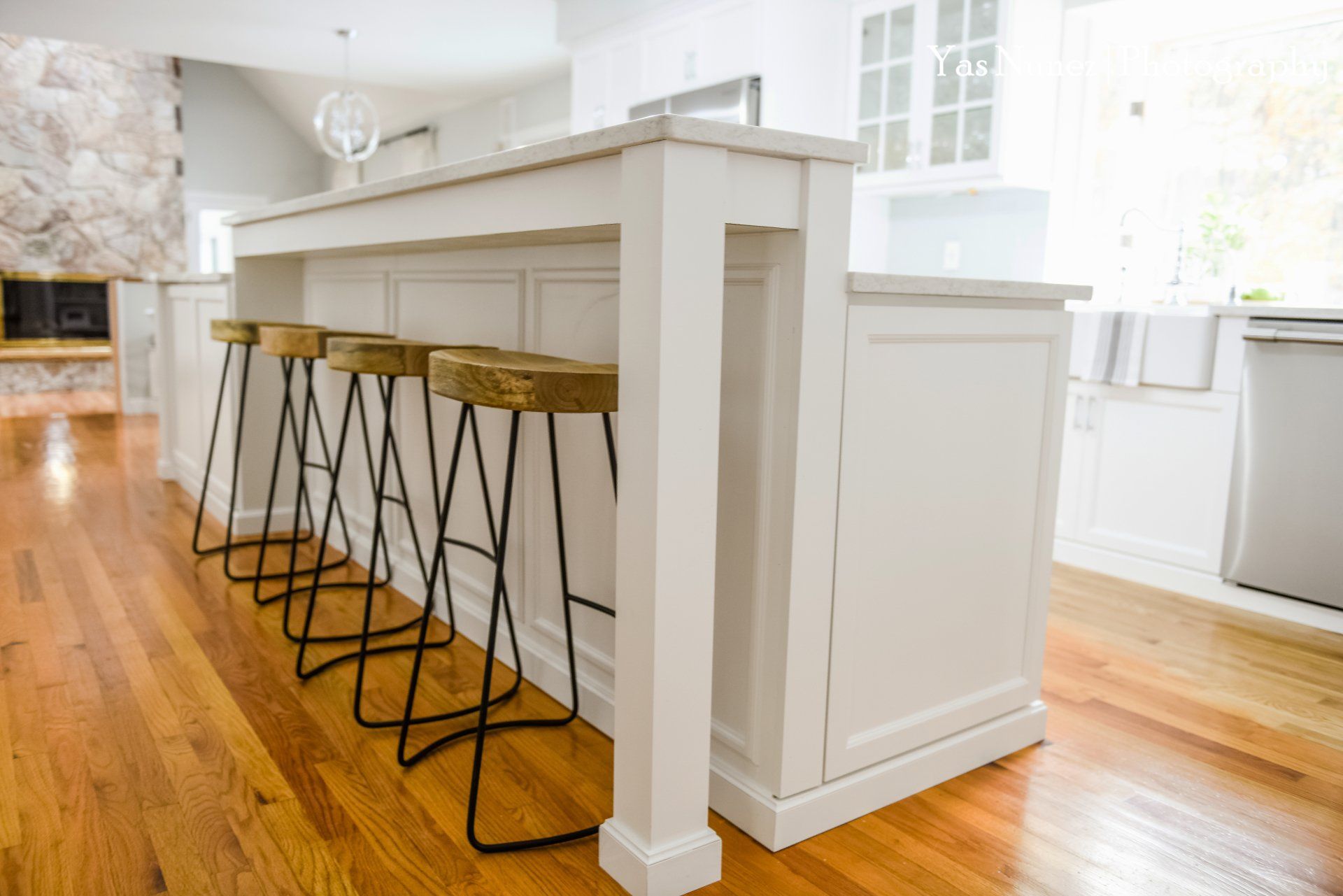 A kitchen with a white island and wooden stools.