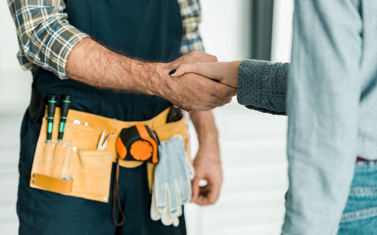 Handshake between a person in work clothes and another person, indoors.