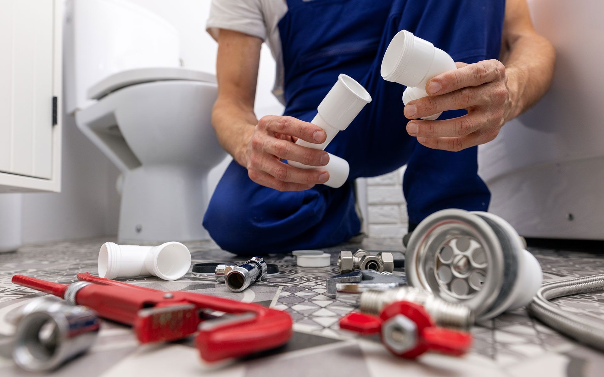 Plumber assembling drain pipes near a toilet, with tools and parts on the floor.
