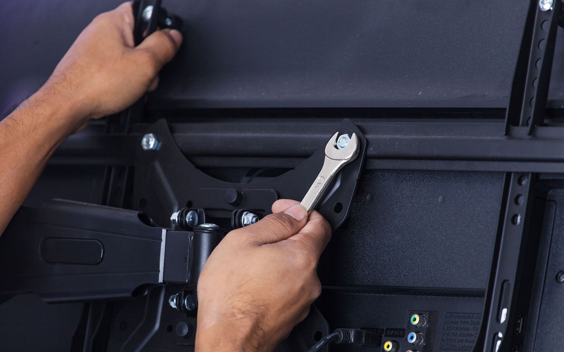 Hands tightening a bolt on a black TV mount with a wrench.
