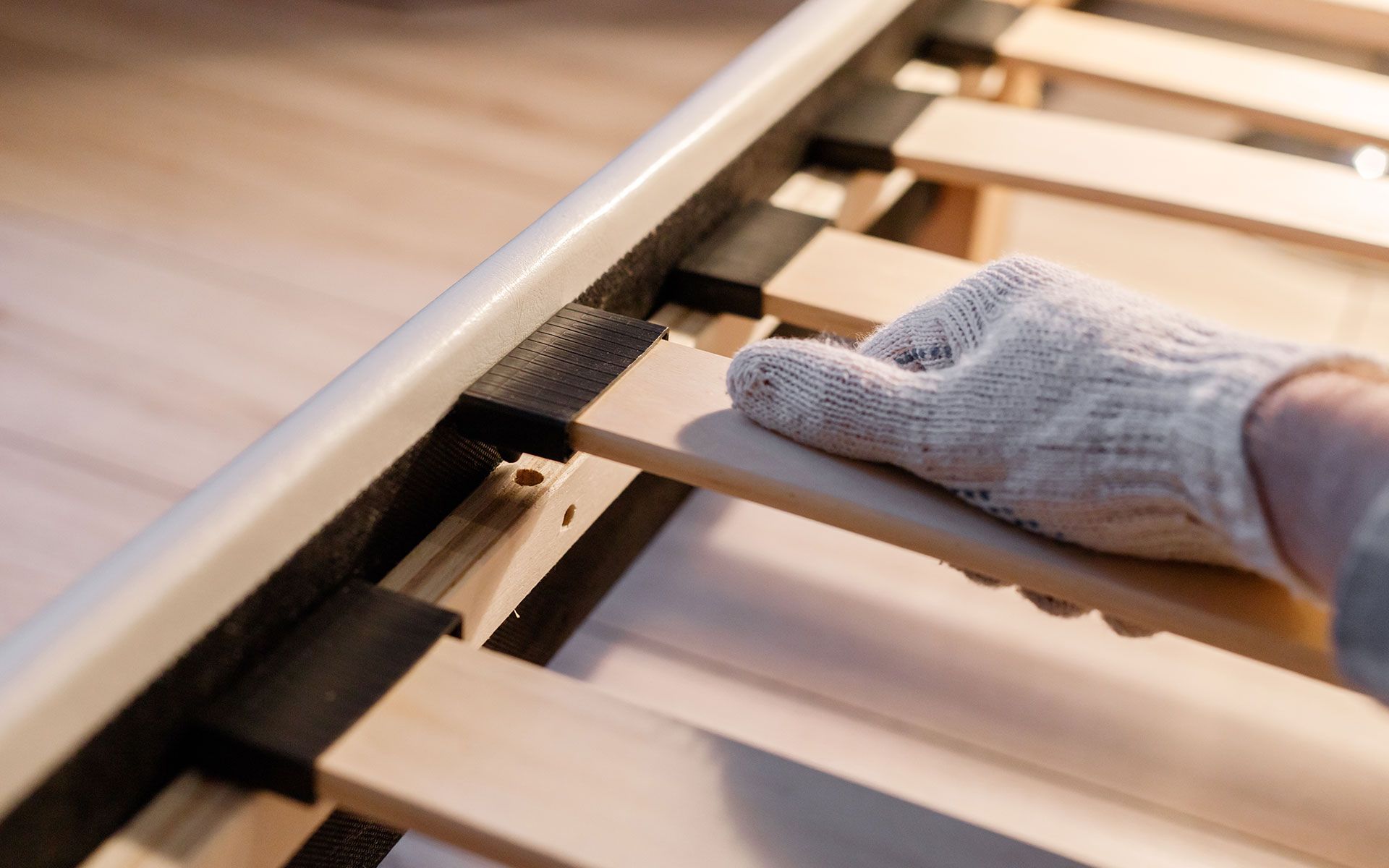 Hand in glove placing a wooden slat on a bed frame.