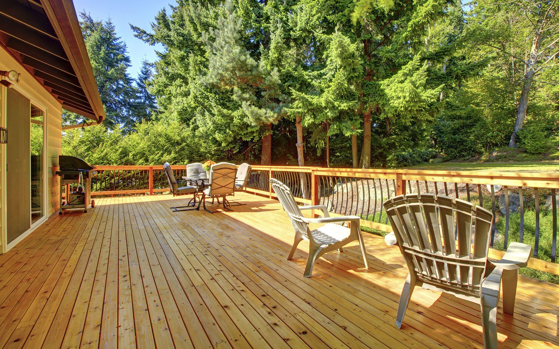 Wooden deck with patio furniture overlooking a green yard and tall trees.