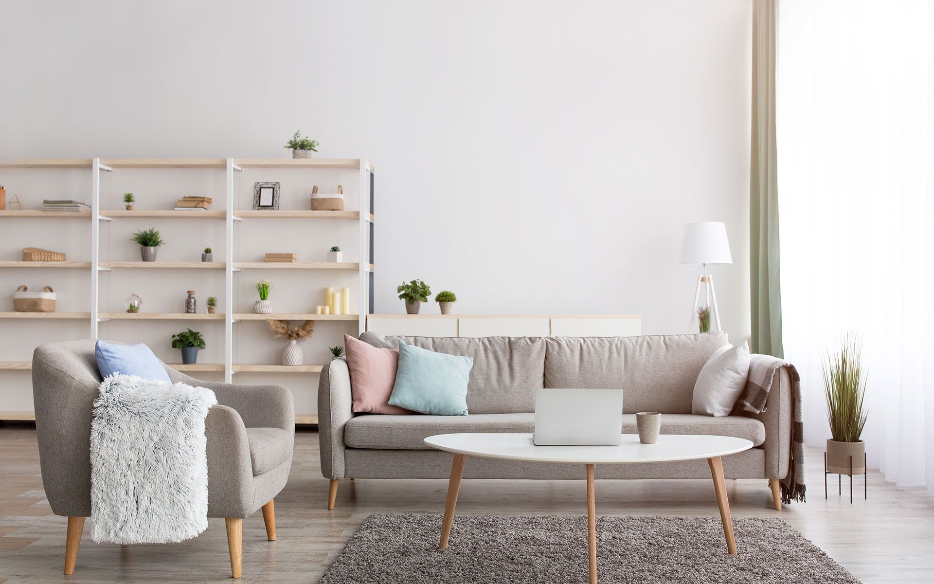 Living room with light-colored sofa, armchair, and shelves against a white wall; coffee table, rug, and window.