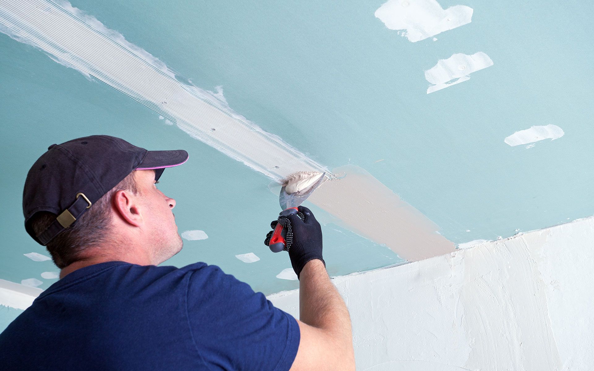 Person applying joint compound to a ceiling with a trowel; mesh tape visible.
