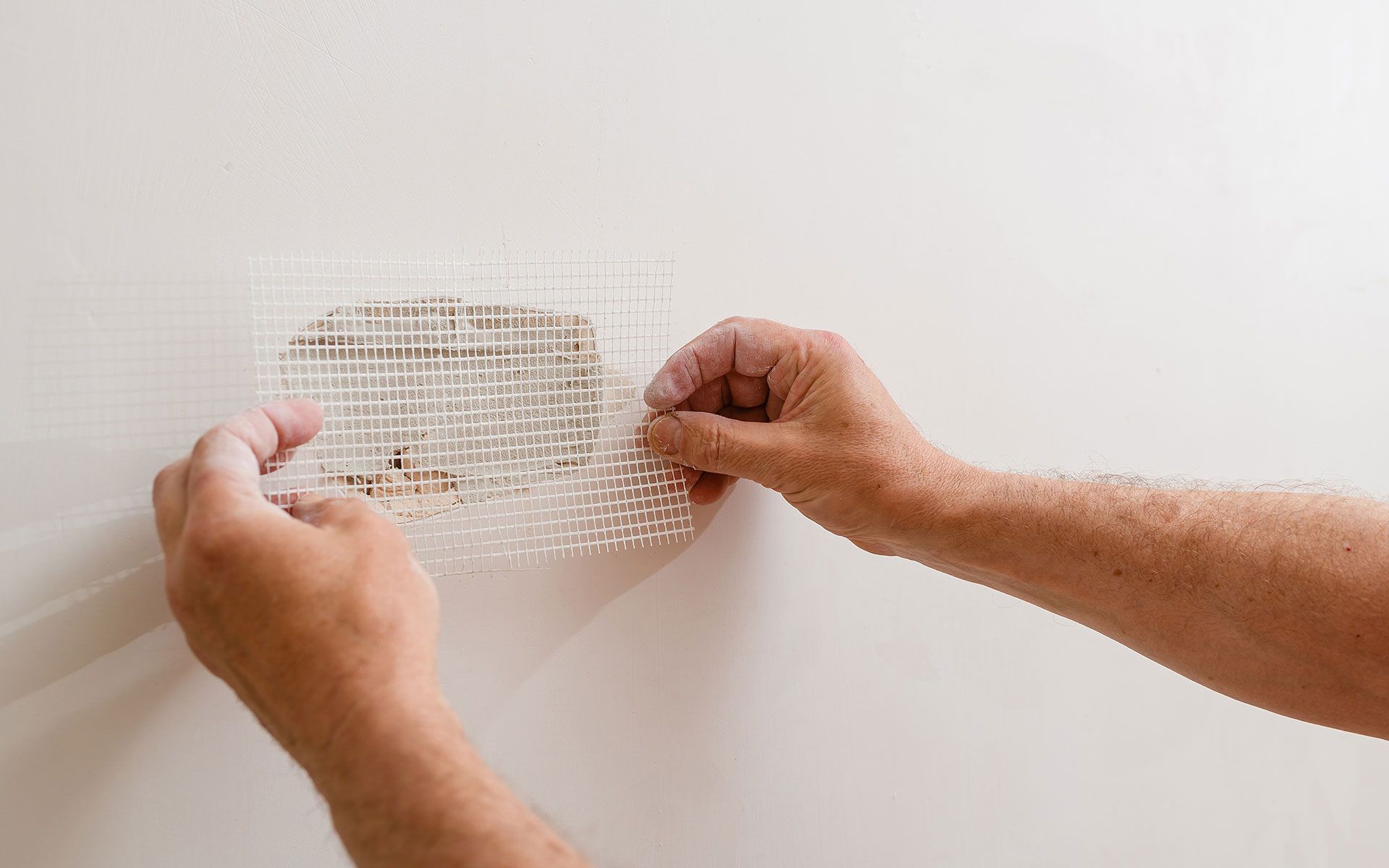 Hands applying mesh patch over damaged wall.