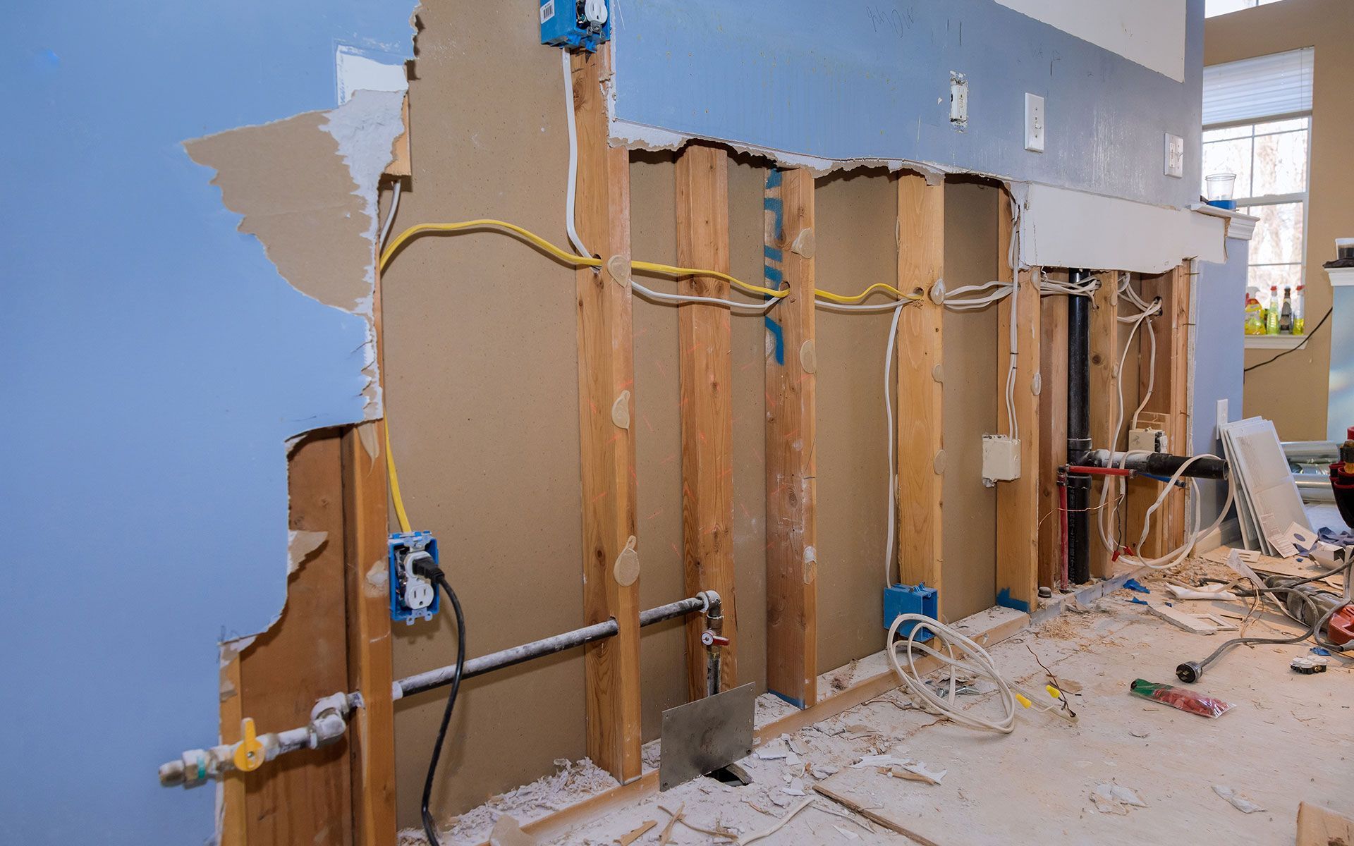 Wall under construction, showing exposed wooden frame, electrical wiring, and plumbing.