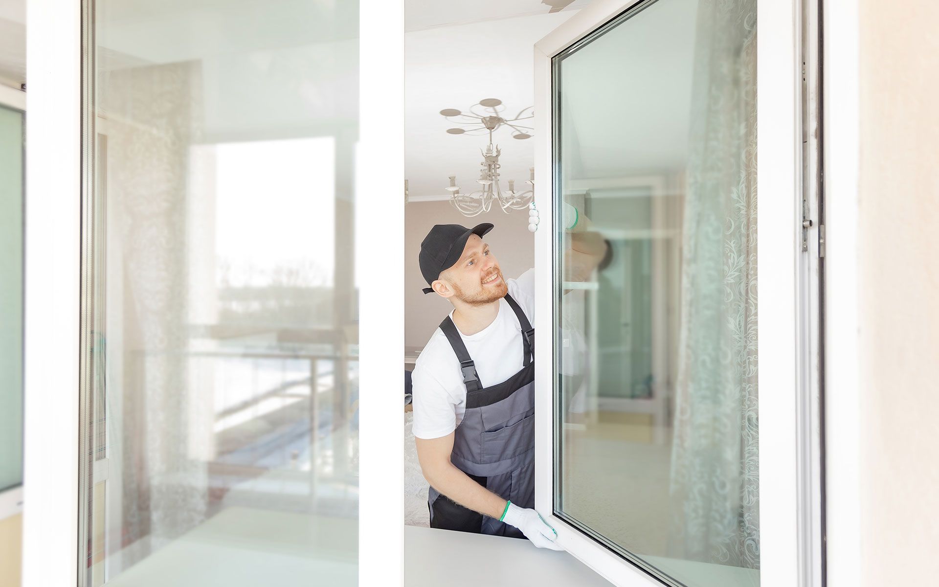 Man in overalls cleaning a window, looking up. Interior shot.