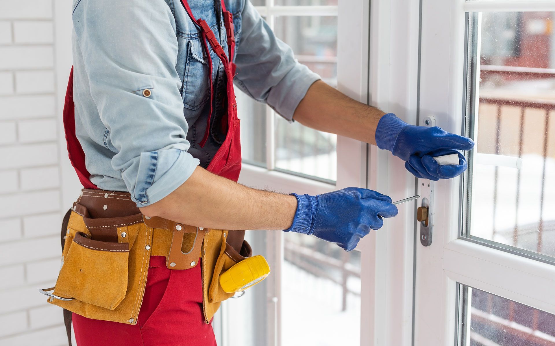 Person wearing gloves and tool belt, using a key to unlock a white door.