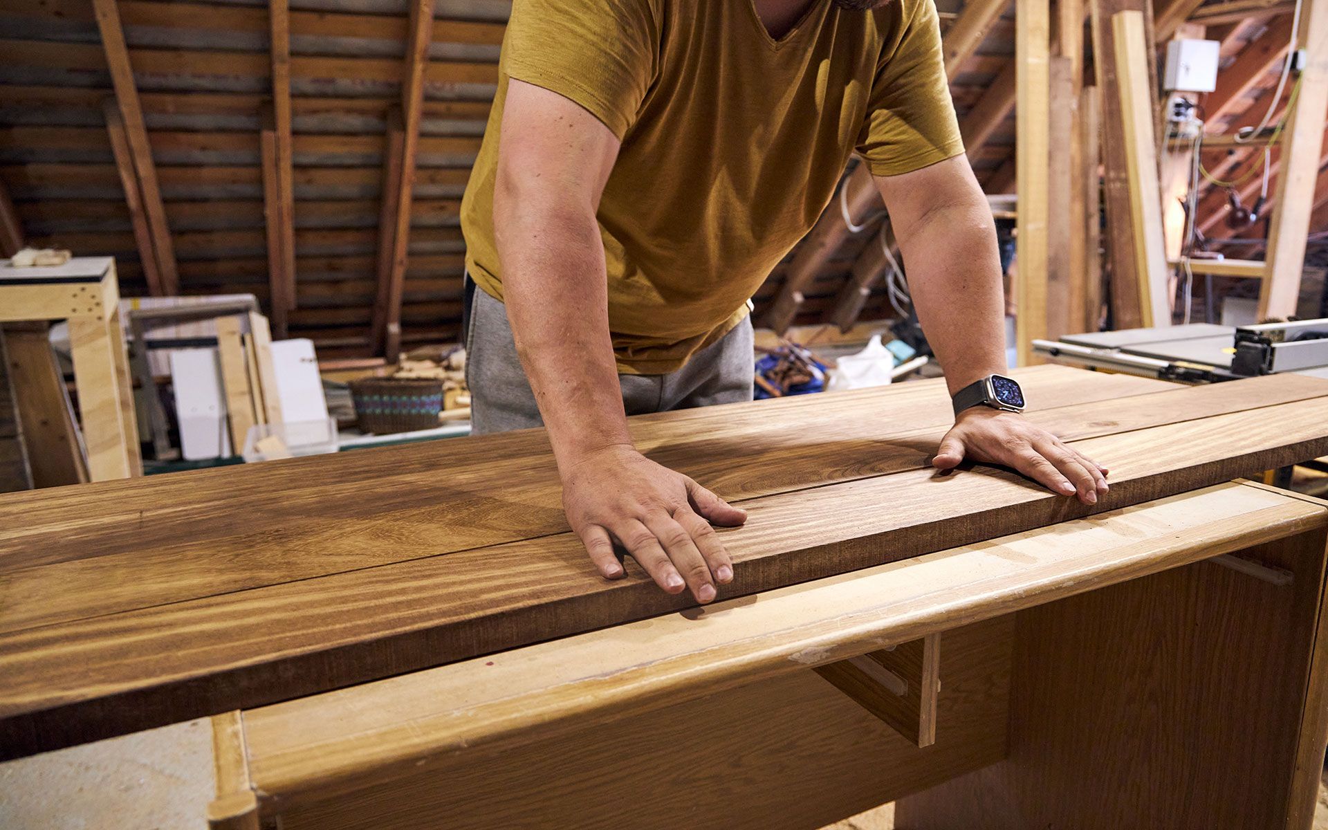 A person in a workshop places hands on wooden planks.