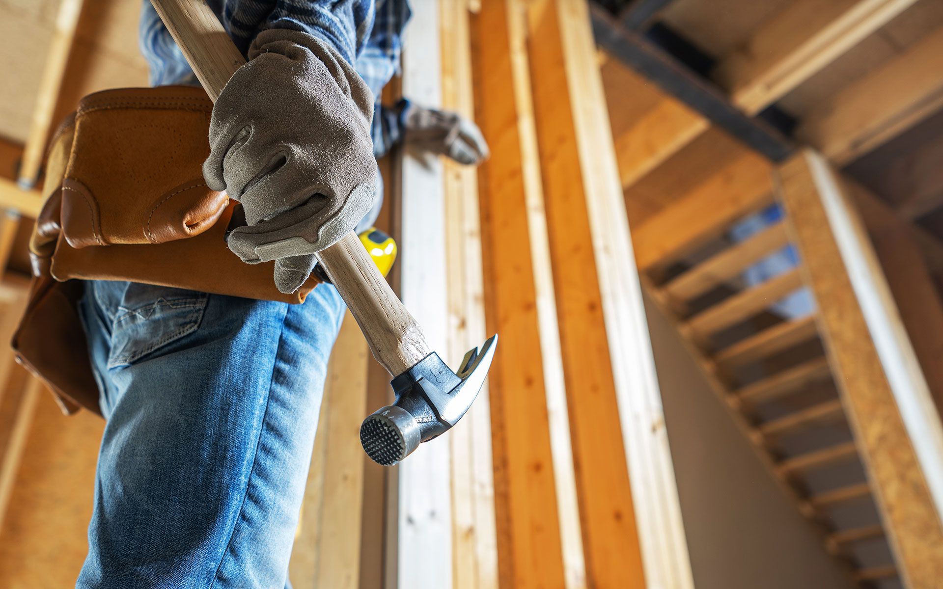 Construction worker holding hammer in a wood-framed building.