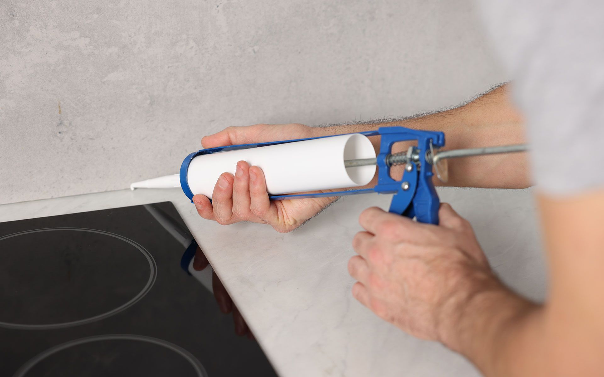 Person applying sealant with a caulking gun near a countertop and stove.