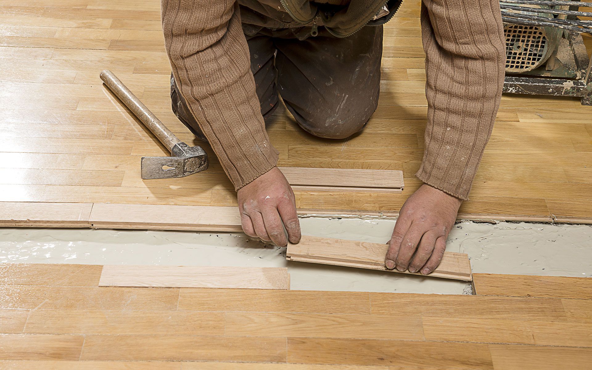Person installing wooden floorboards, hands placing pieces over adhesive.