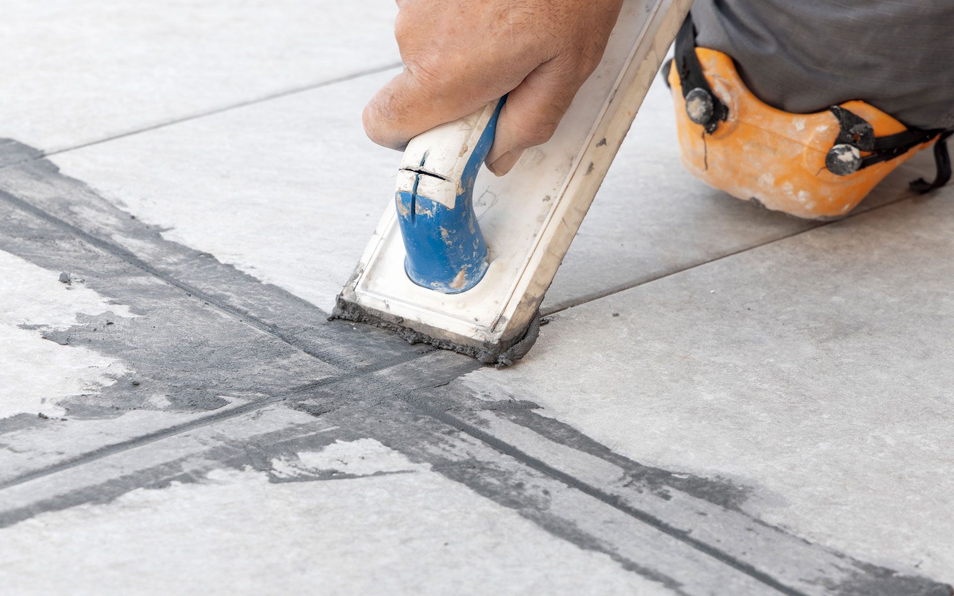 Person using a grout float to apply grout between tiles on a floor.
