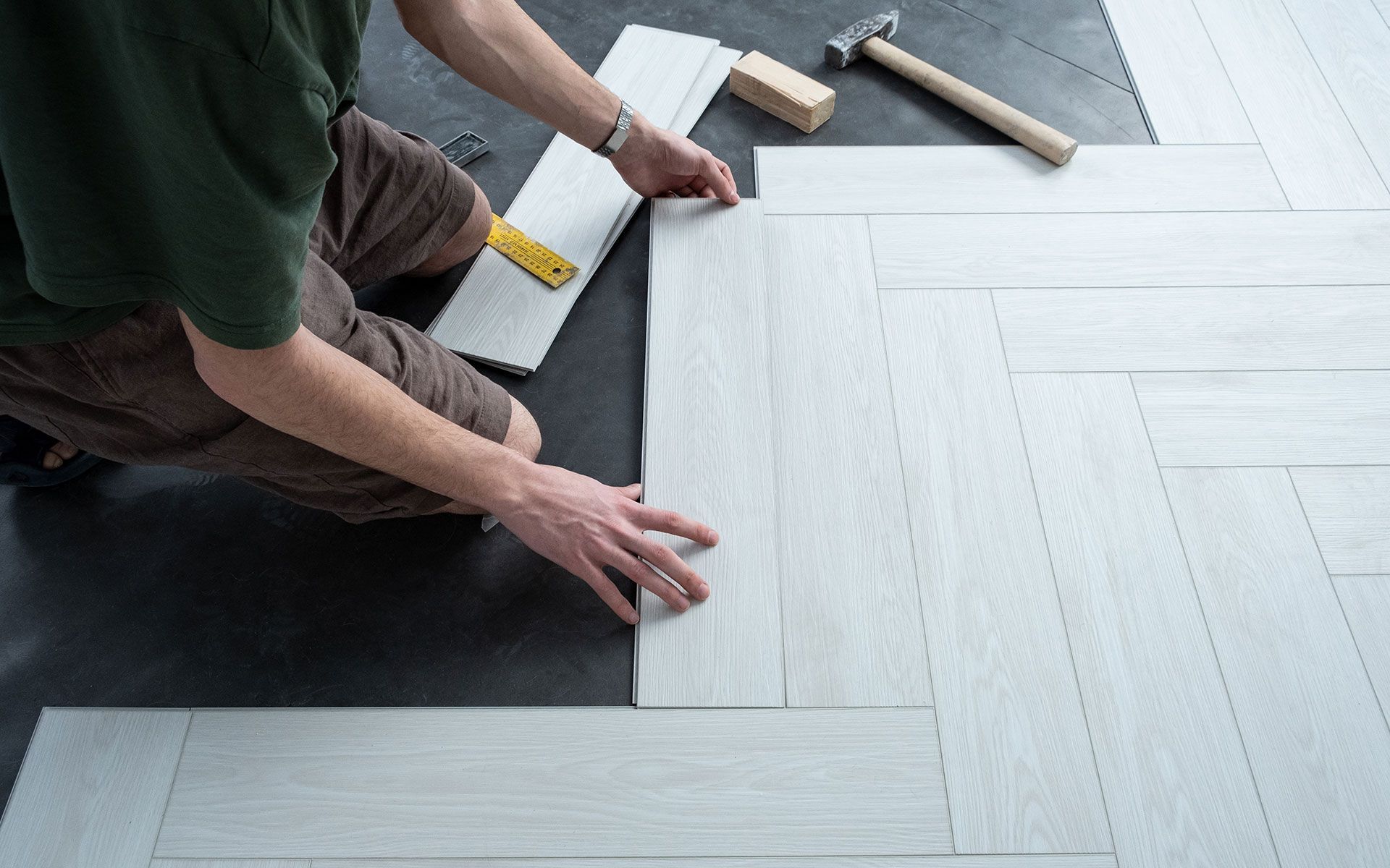 Person installing light-colored wood flooring in a herringbone pattern with tools nearby.