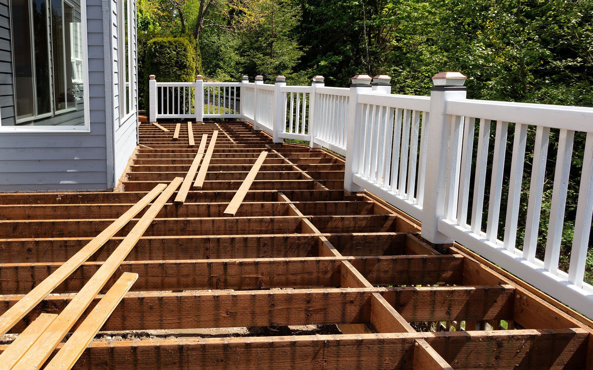 Deck under construction, with white railing and visible wooden frame. Boards are partially laid.
