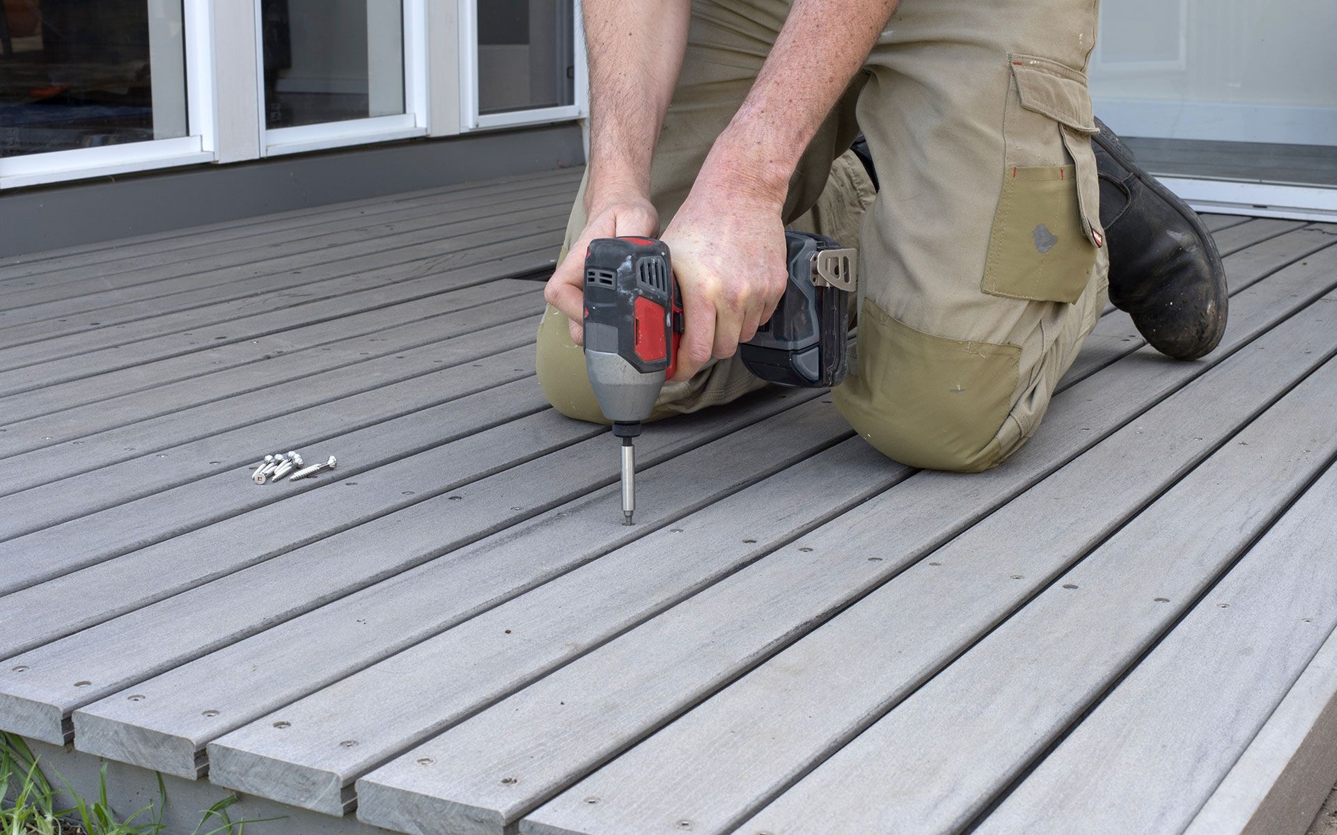 Person using a drill to install screws on a gray deck.