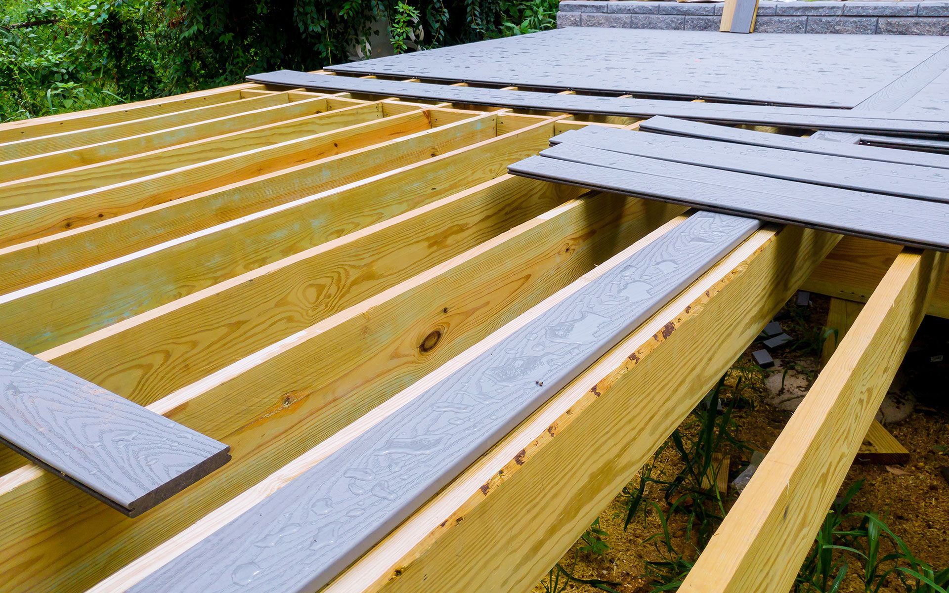 Wooden deck frame with gray composite decking being installed.