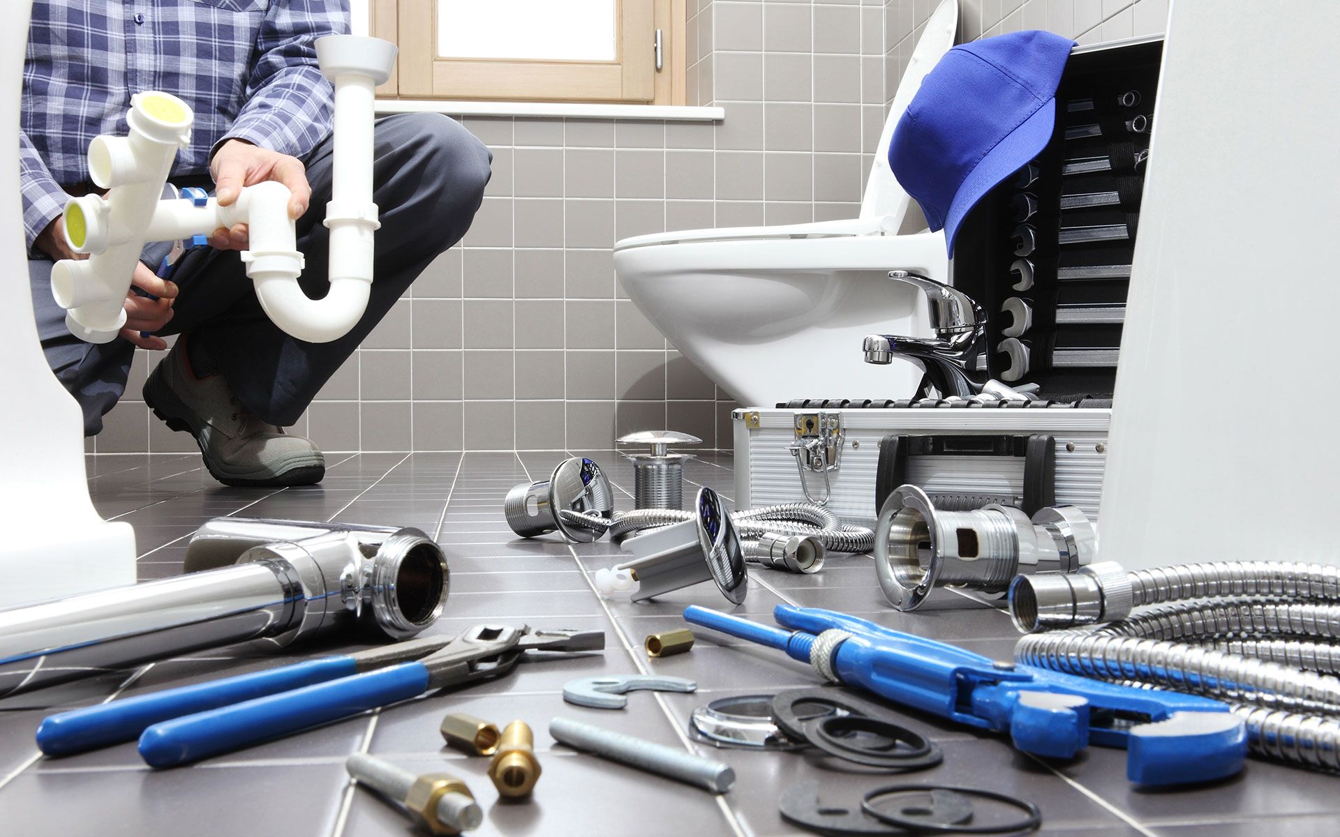 Plumber in bathroom, assembling plumbing parts near a toilet. Tools and parts scattered on the tiled floor.