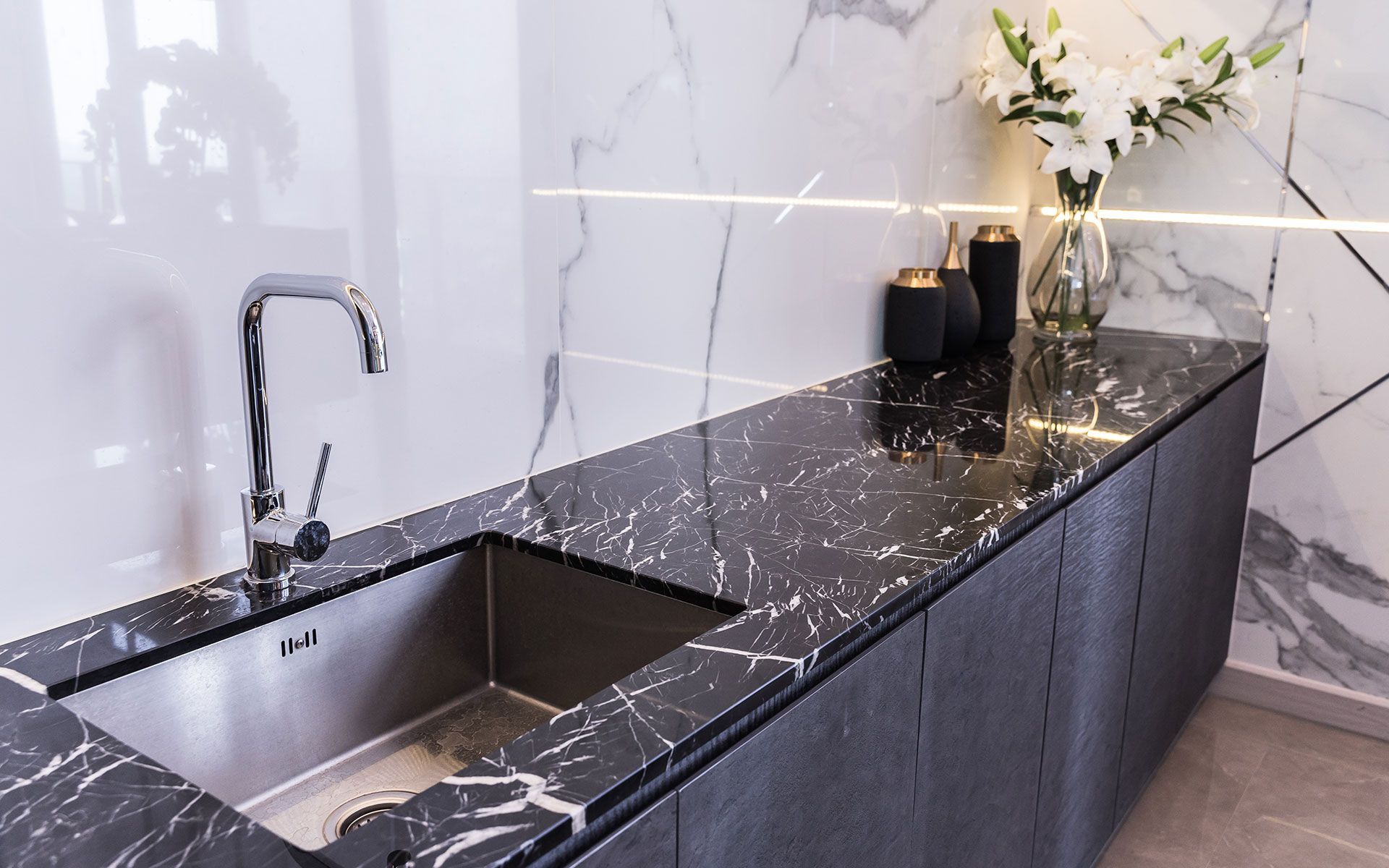 Kitchen countertop with black marble, stainless steel sink, and white marble backsplash.