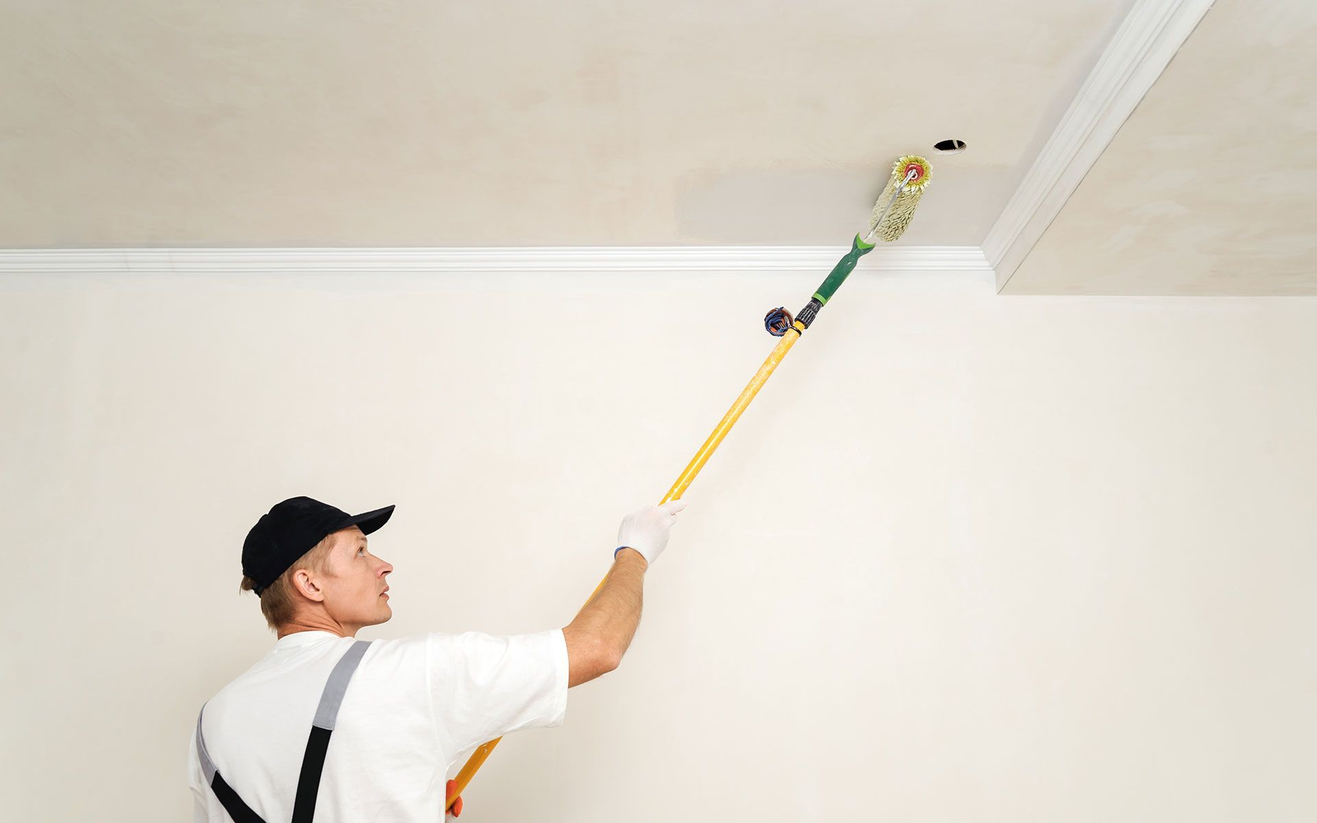 Painter using a roller on a ceiling, white paint, interior room, painting trim.