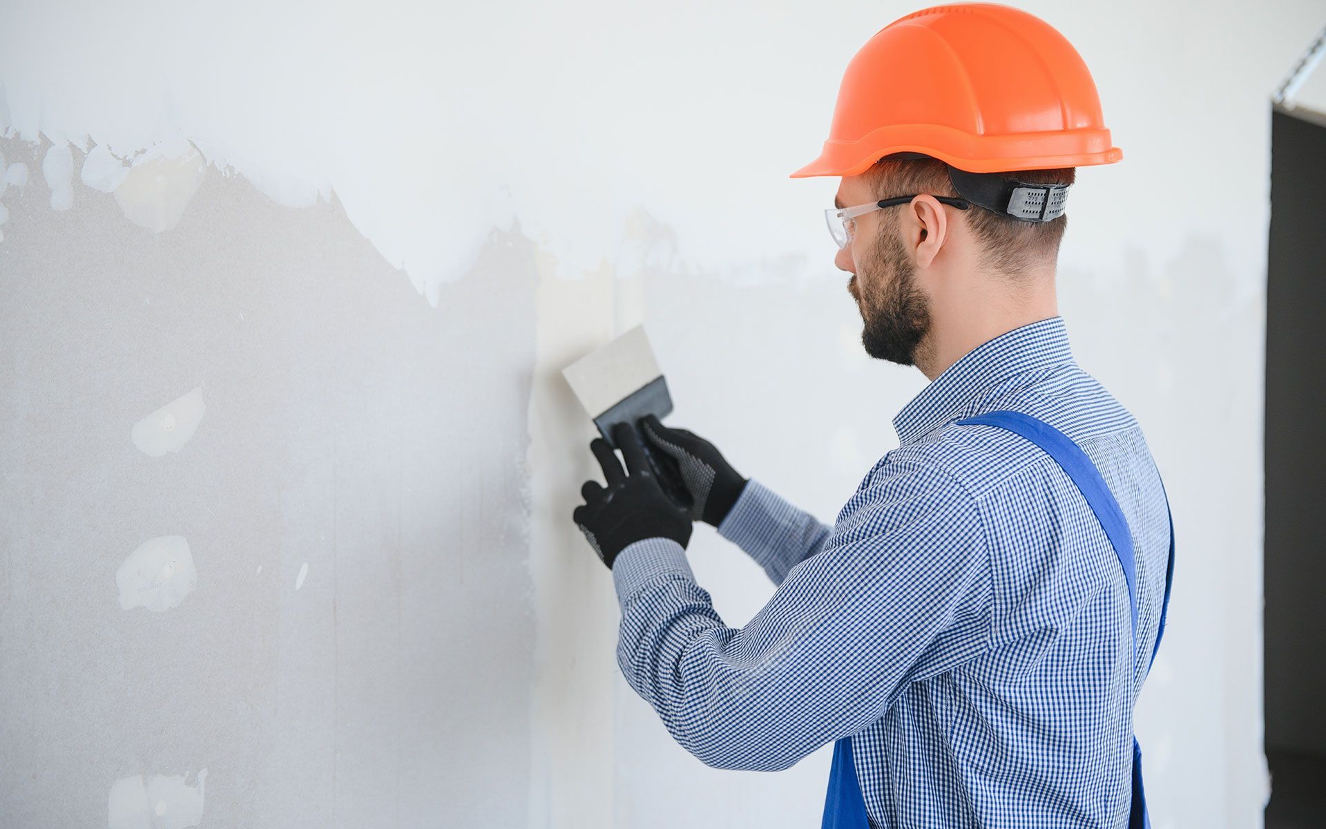 Construction worker, orange hard hat, smoothing wall with trowel.
