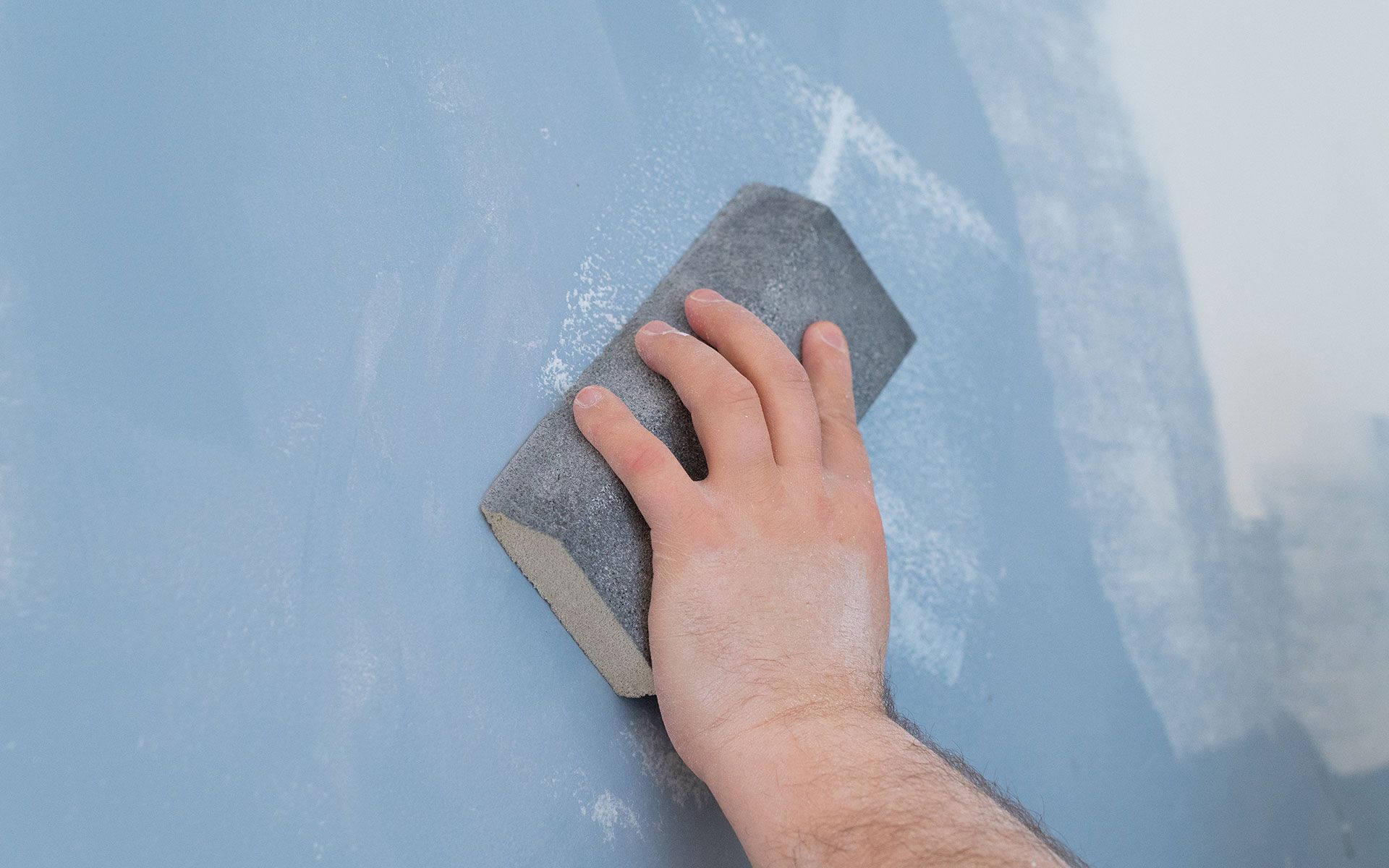 Hand sanding a blue wall with a sanding block.