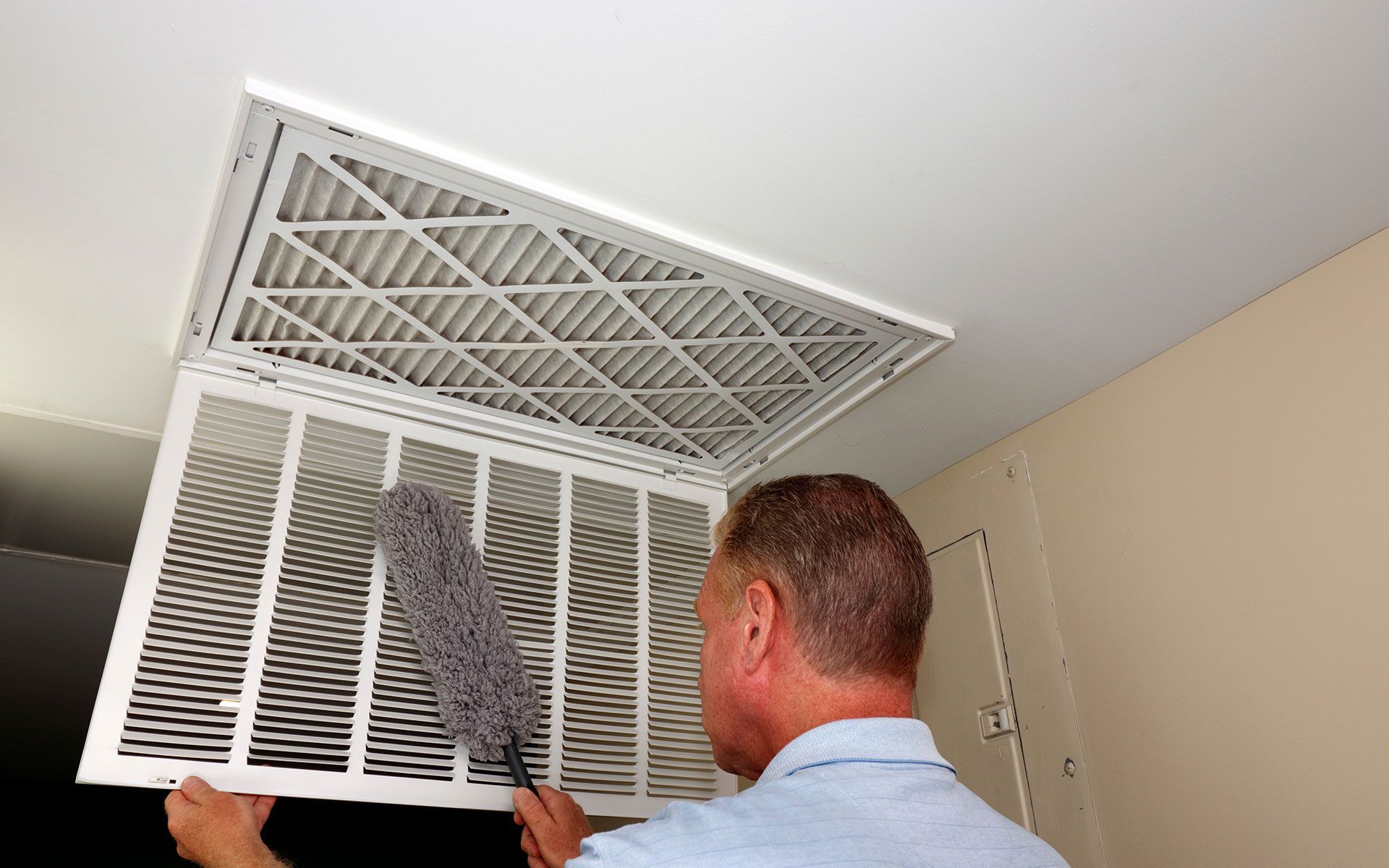 Person dusting an HVAC vent filter in a white ceiling.