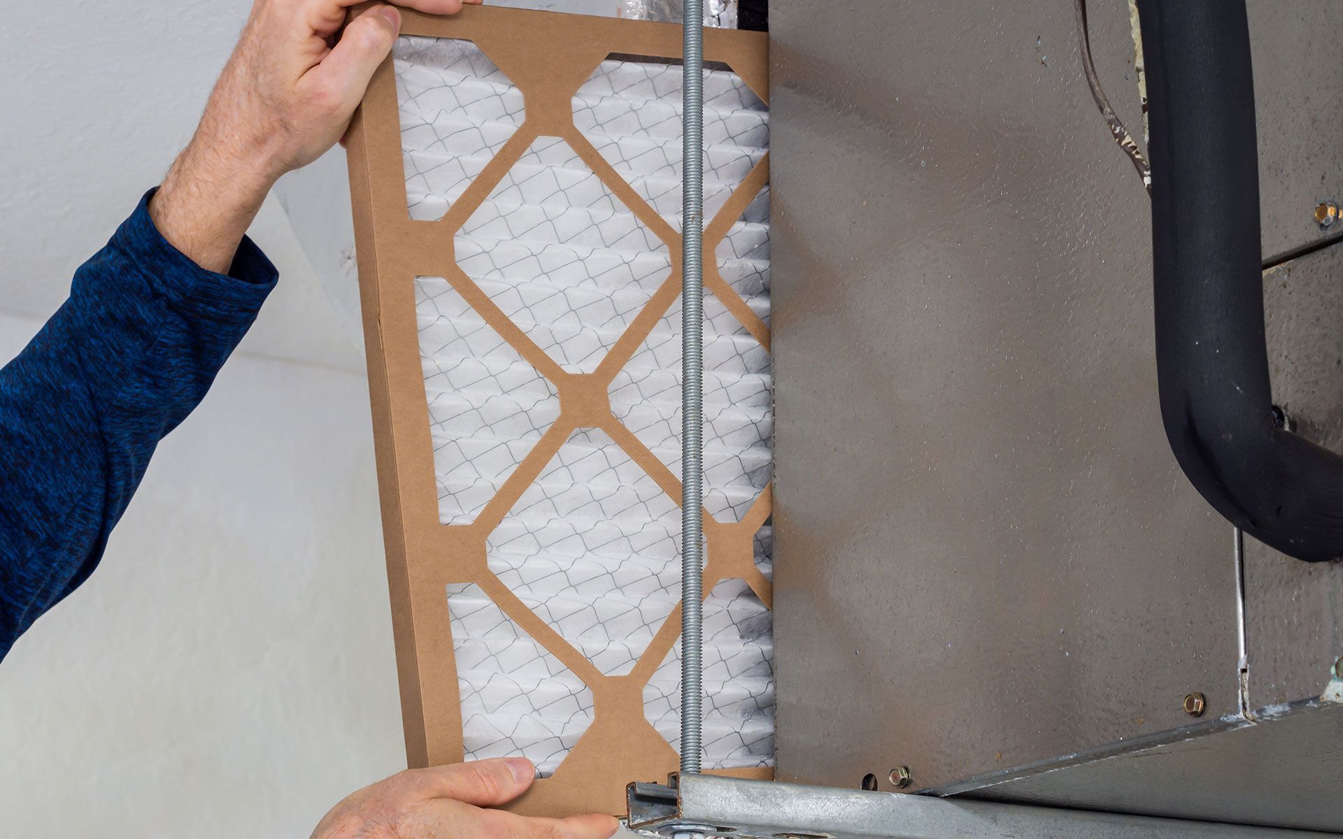 Person replacing an air filter in an HVAC system; hands holding filter next to its housing.