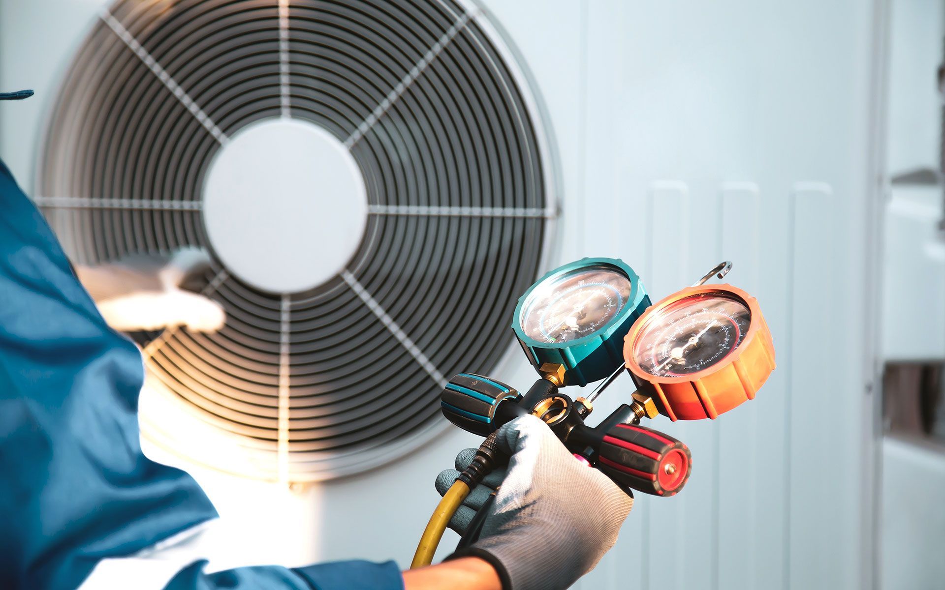 HVAC technician servicing outdoor unit with gauges, wearing gloves.