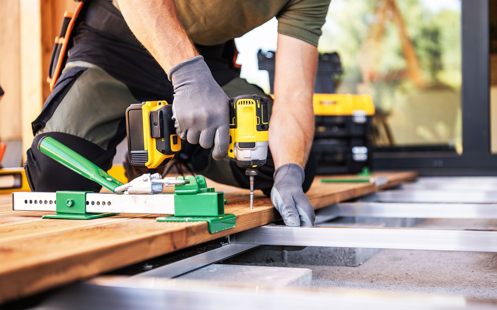 Person cleaning a blue, kidney-shaped swimming pool with a long brush on a sunny day.