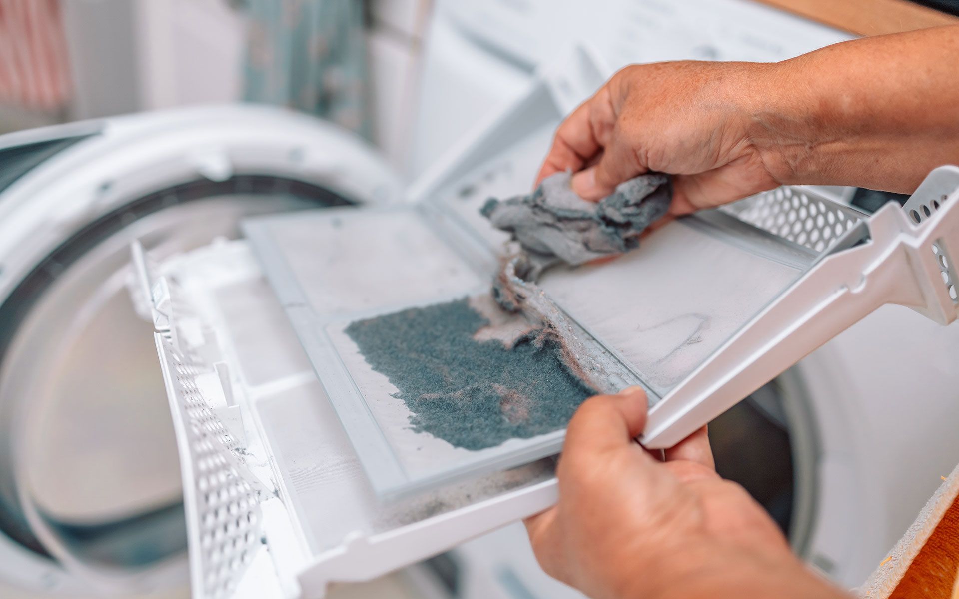 Hands cleaning a dryer lint filter filled with gray lint.