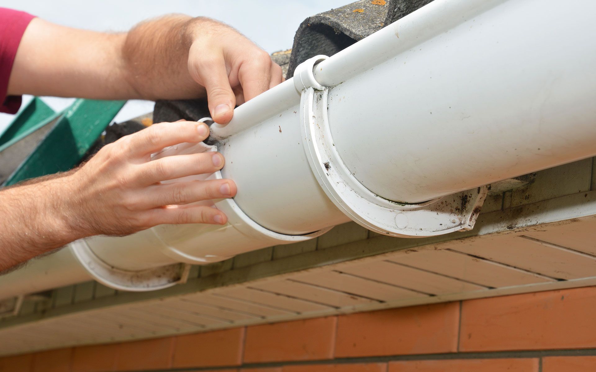 Person installing a white gutter on a house, hand adjusting.