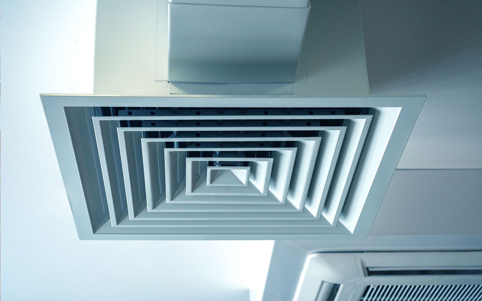 Square, layered air vent on a white ceiling, connected to a rectangular duct.